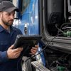 Tehnician cu tabletă de diagnoză conectată la conectorul Deutsch verde al unui camion în service