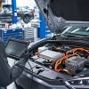 Tehnician cu tabletă de diagnoză la o mașină electrică cu cabluri de înaltă tensiune portocalii