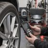 Tehnician cu o unealtă TPMS handheld lângă janta unei mașini, într-un service de anvelope